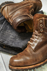 A pair of hiking boots with multiple stitching in brown leather along with folded jeans on a light wooden surface