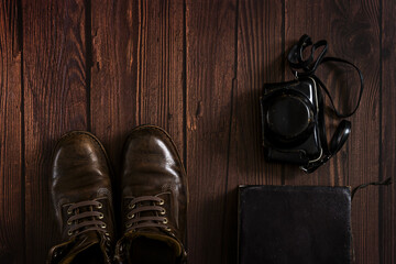 a composition with leather boots, an old book and a camera obscura case on  a dark wooden surface