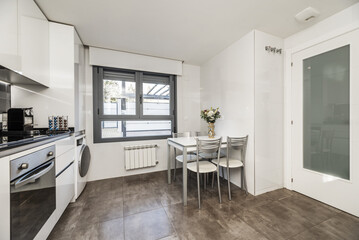 White dining table with metal chairs in the kitchen of a two-story house with many appliances and dark stoneware floors