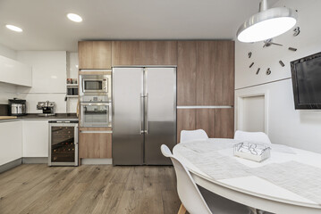 Image of a furnished kitchen in a single-family home with integrated stainless steel appliances covering a wall with light wood furniture