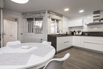 furnished L-shaped kitchen in a detached house with integrated stainless steel appliances, extractor hood and white wooden circular dining table
