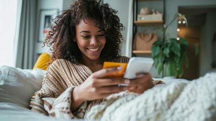 Cheerful woman relaxing in bed with a smartphone in a cozy, homely setting with warm tones, possibly representing a leisurely morning or personal time.