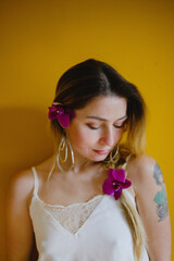 Portrait of a blonde girl against a yellow wall. Close-up with an orchid in her hair