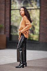 Beautiful Asian woman fashion model in the latest trends layered knit sweater, leather pants, high heeled boots Standing on a city street
