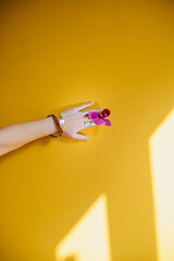A hand with an orchid flower against a yellow wall.