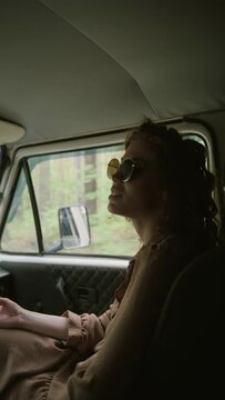 Vertical shot of young cheerful woman in casualwear and sunglasses explaining something to driver of camper van during communication on their way to countryside