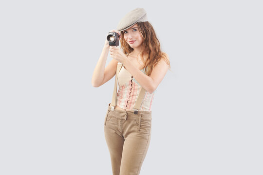 Smiling girl holding an old-fashioned retro video camera, dressed in vintage style. Video maker service or influencer social media content creator. Second hand store concept. Isolated on background