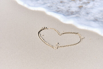 Fototapeta na wymiar Foamy wave, washing over light sand with outline drawing of heart symbol. Tropical beach.
