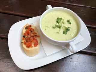 A bowl of creamy zucchini soup garnished with fresh garden cress, served with a slice of tomato...