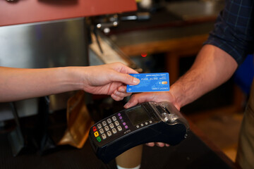 Close-up of hands exchanging credit card and electronic payment terminal over cafe counter. card transaction in progress, showing interaction between customer, barista, and POS machine.