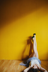 Portrait of a blonde girl against a yellow wall. He is lying on the floor with his feet in his shoes up