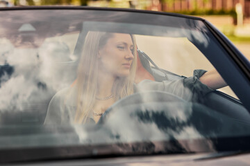 An attractive woman is sitting in a convertible car. Summer holidays, traveling by car