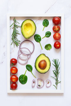 Bright composition with white picture frame with assortment of salad ingredients on white marble table top view, healthy tasty food concept. Vertical image.

