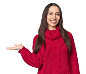 Young Caucasian woman in cozy red sweater on studio background showing a copy space on a palm and holding another hand on waist.
