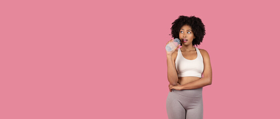 Curious black woman drinking water posing in sportswear, pink backdrop, free space