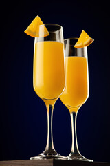 Champagne flutes with orange juice garnished with orange wedges against a black background.
