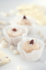 Three coconut truffles topped with almonds, amidst white chocolate chips and a nutty bar