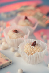 Three coconut truffles topped with almonds, amidst white chocolate chips and a nutty bar