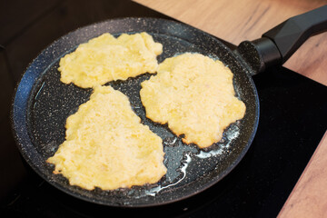 Golden-brown potato pancakes frying in a speckled non-stick pan on a hob.