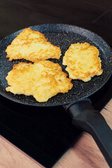 Golden-brown potato pancakes frying in a speckled non-stick pan on a hob.