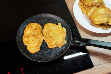 Golden-brown potato pancakes frying in a speckled non-stick pan on a hob.