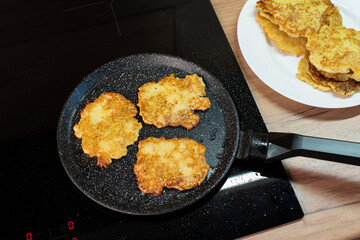 Golden-brown potato pancakes frying in a speckled non-stick pan on a hob.