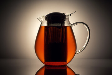 Elegantly designed glass teapot with amber-colored tea, glowing against a background with a reflective surface.