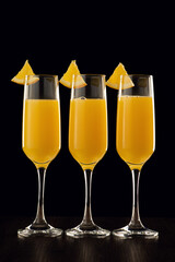 Champagne flutes with orange juice garnished with orange wedges against a black background.