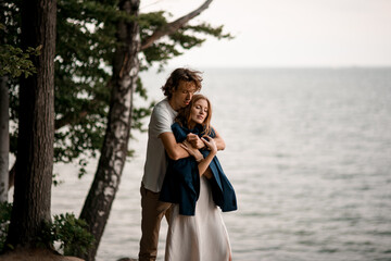 Husband hugs his pretty slender wife tightly from the back, wearing his jacket on her shoulders
