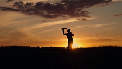 Child boy runs through meadow with toy airplane and throws airplane into sky. Silhouette. Teenager...