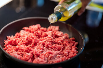 adding olive oil to mince meat in frying pan.