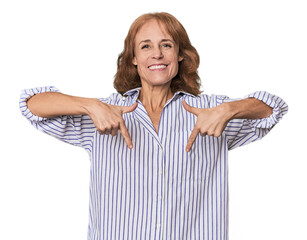 Redhead mid-aged Caucasian woman in studio points down with fingers, positive feeling.