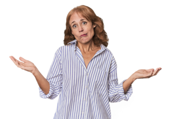 Redhead mid-aged Caucasian woman in studio doubting and shrugging shoulders in questioning gesture.