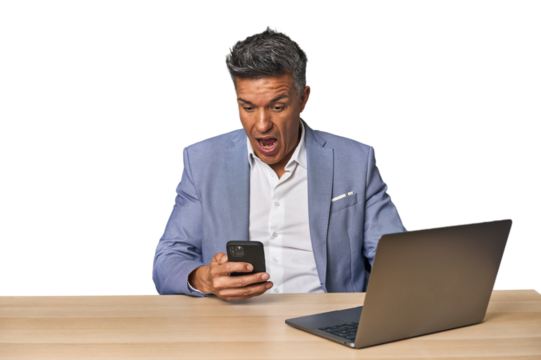 middle age latin man surprised working with his laptop and phone