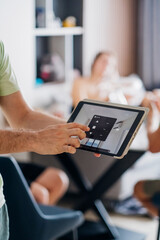 Man's hand is shown adjusting a smart home control panel on a digital tablet, symbolizing the intersection of technology and daily life.