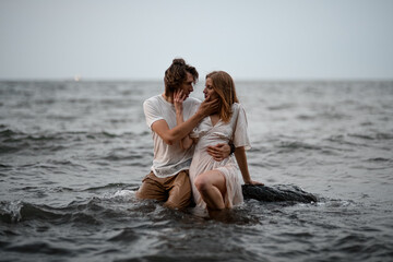 Young couple sits in the water on a rock and looks into each other's eyes