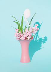 Beautiful fresh pink hyacinth flowers in a vase and white Easter egg. Copy space. Light blue background. Front view. Minimal springtime holiday concept.