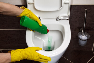 Cleaning and disinfecting the toilet. A cleaner wearing yellow protective rubber gloves treats a toilet with a cleaning agent