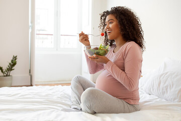 Beautiful black pregnant woman with radiant smile eating fresh vegetable salad