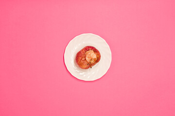 Rotten bitten apple on a saucer, on a pink background, close-up. Studio photo....