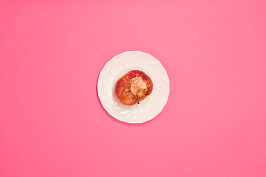 Rotten bitten apple on a saucer, on a pink background, close-up. Studio photo. Advertising/presentation concept.