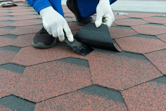 the hands of a worker in white gloves, apply black mastic with a spatula, to repair the soft roof of the roof