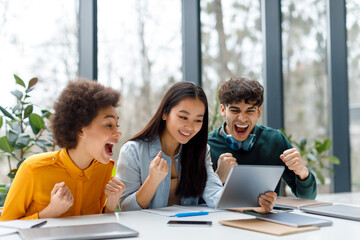 Excited diverse students friends celebrating success with tablet