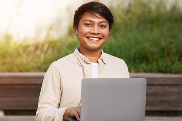 Closeup of cheerful asian guy using computer outdoors