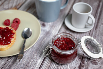 Homemade raspberry jam in glass jar, healthy breakfast with toast, raspberry jam, milk in cup and...