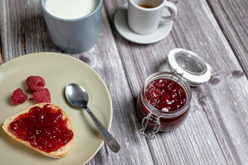 Homemade raspberry jam in glass jar, healthy breakfast with toast, raspberry jam, milk in cup and...