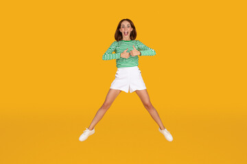 Fototapeta na wymiar Positive young woman jumping over yellow background