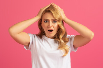 Desperate blonde woman touching head in frustration on pink background