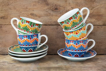 composition of coffee cups and saucers with multicolored patterned decorations on rustic wooden...