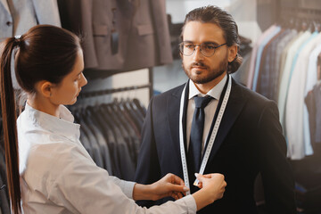 Assistant woman seller taking measurements of young handsome businessman in suit shop. Concept...